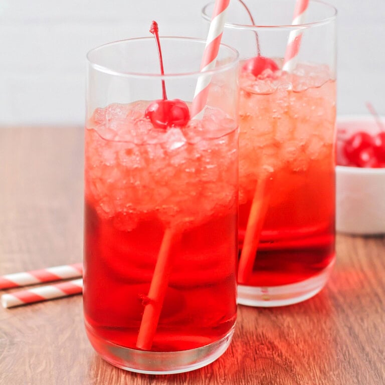 Shirley temple drink image with straws, ice and cherries in the cups.
