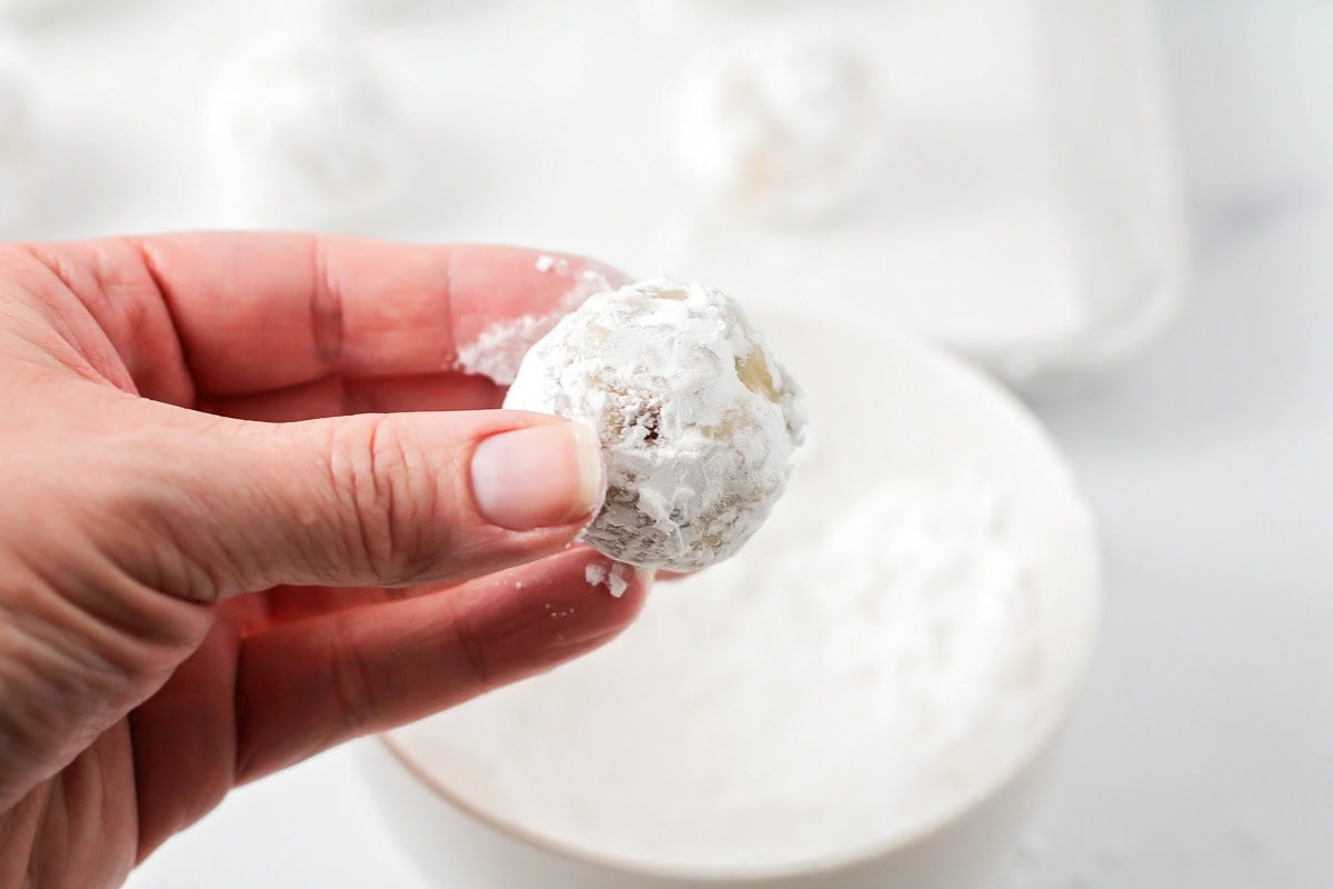 Snowball cookies being dipped in powdered sugar.