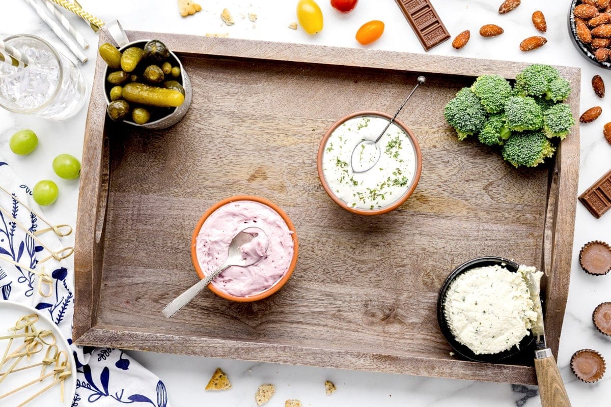 A process photo of building a charcuterie board with just three dips and broccoli on the board. 