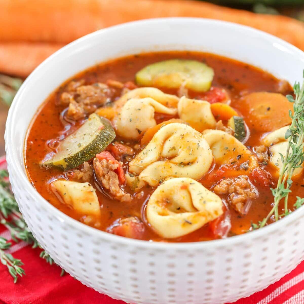 Tortellini soup recipe poured into white bowl with fresh herbs on the side.