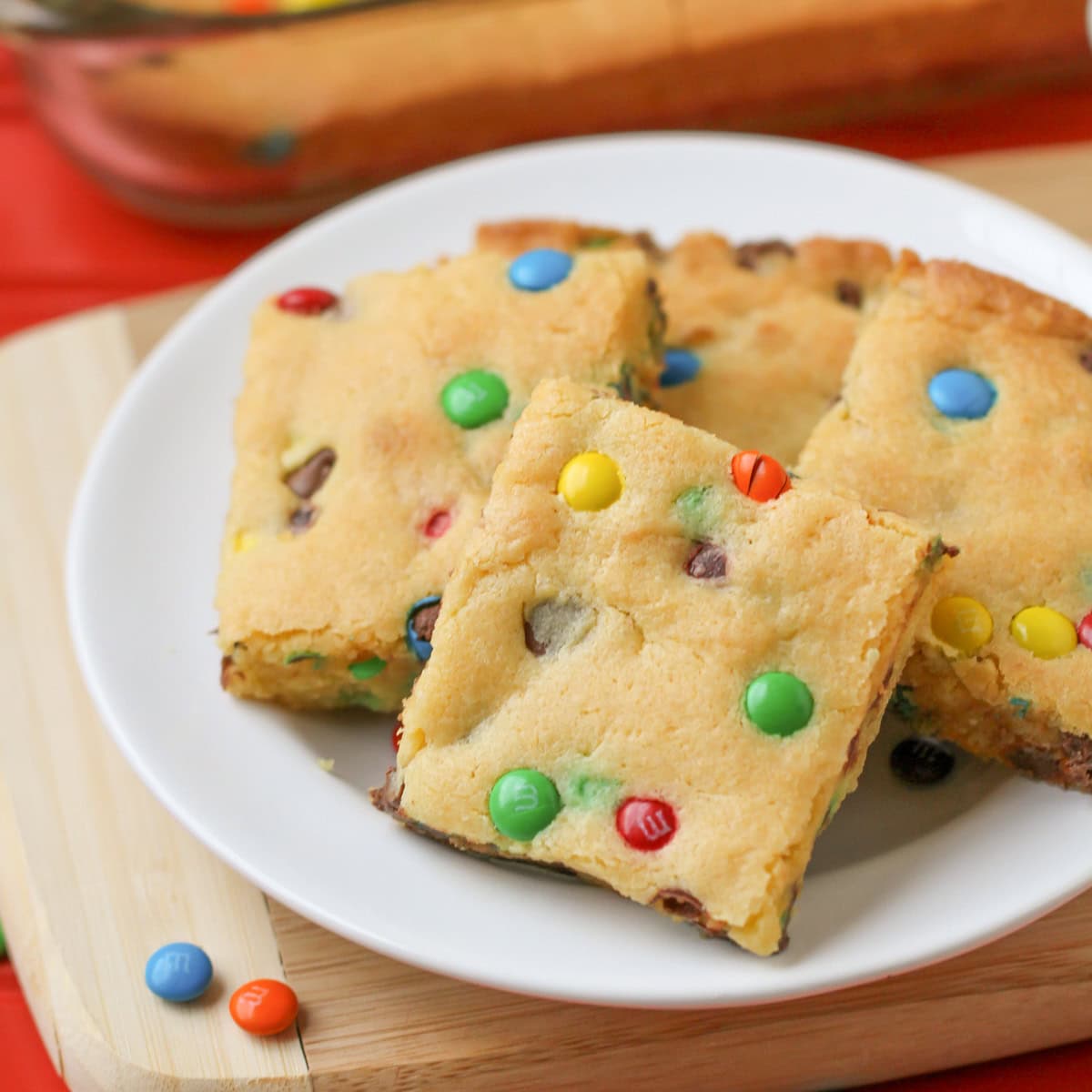 Cake mix cookie bars with M&Ms on top, cut and placed on white plate.