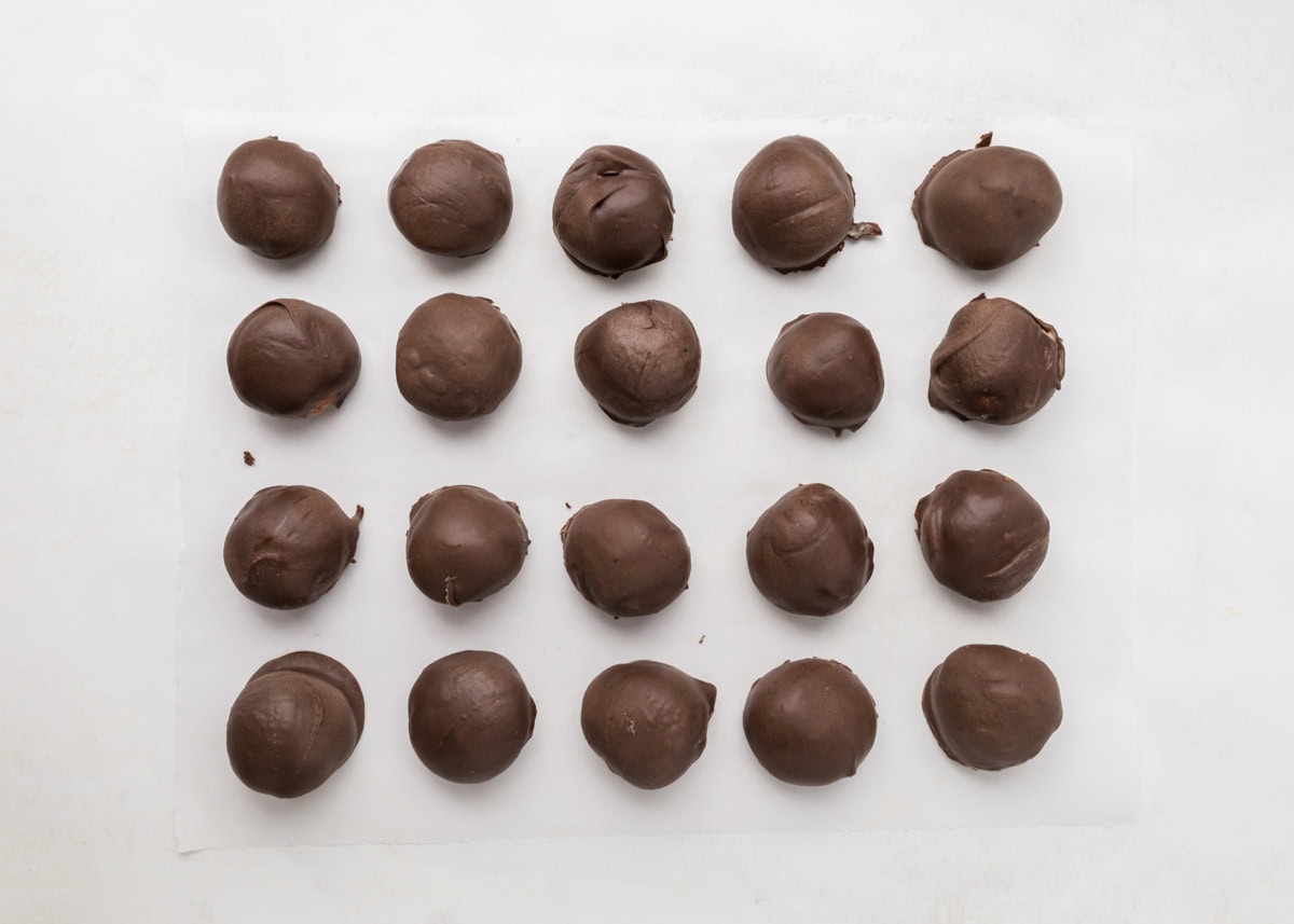 Chocolate dipped cheesecake bites on parchment paper.