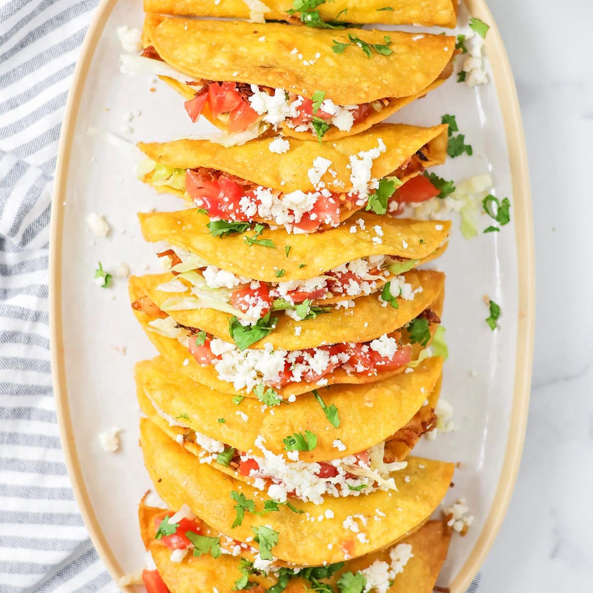 Close up image of several homemade chicken tacos on white platter.