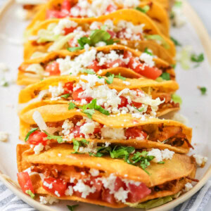 Chicken Tacos stacked on white platter with dish cloth.