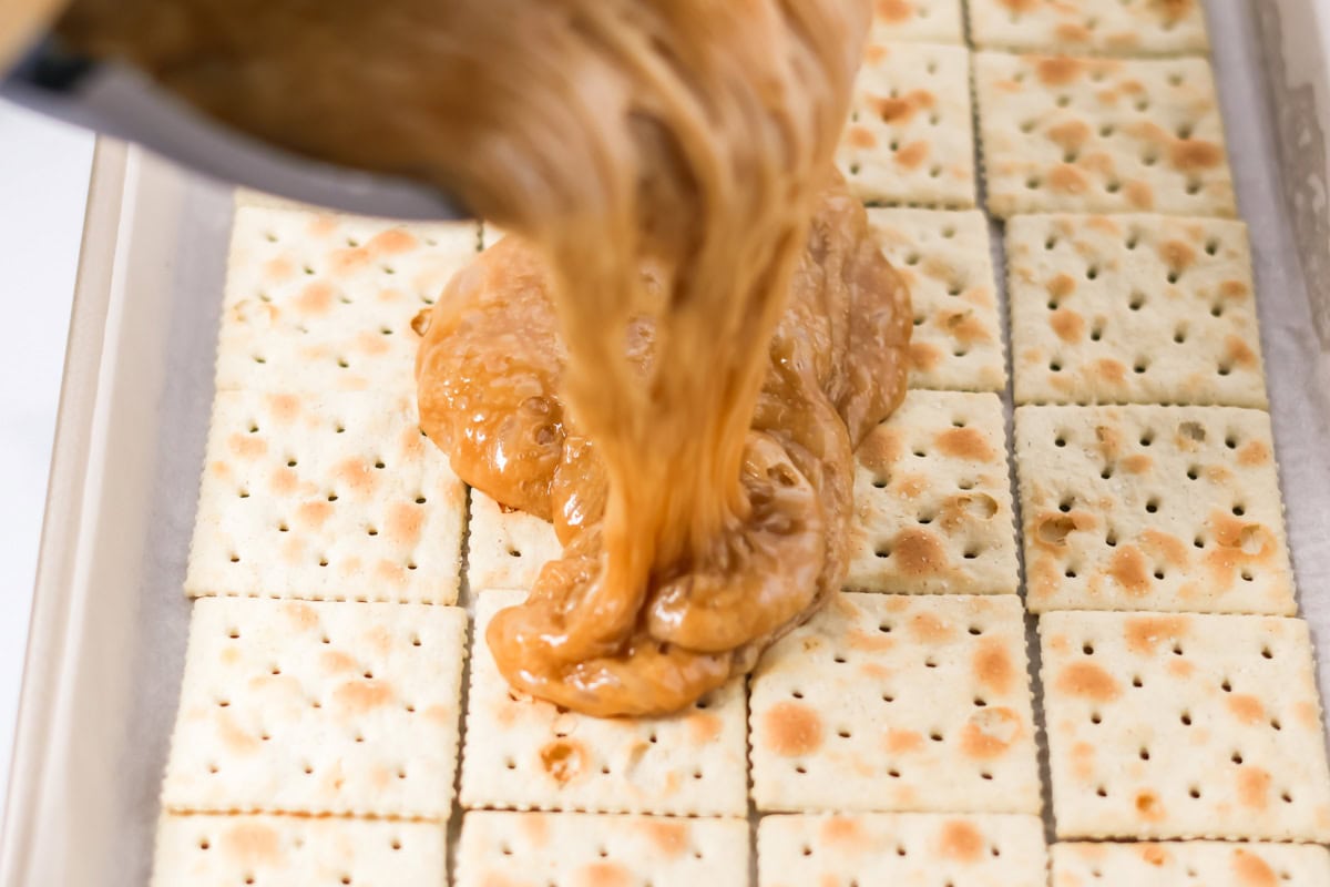 Hot toffee mixture being poured over saltine crackers.