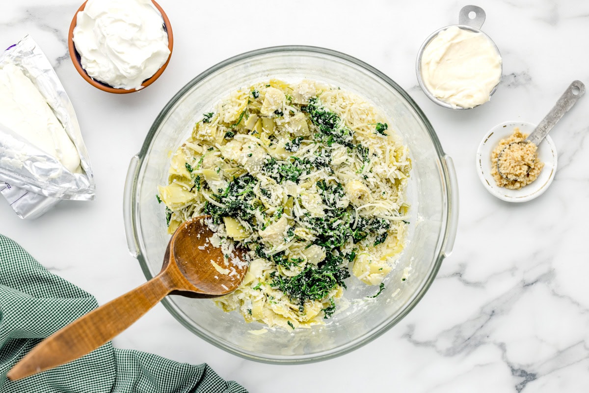 Spinach, artichokes, and cheese mixed together in a glass bowl.