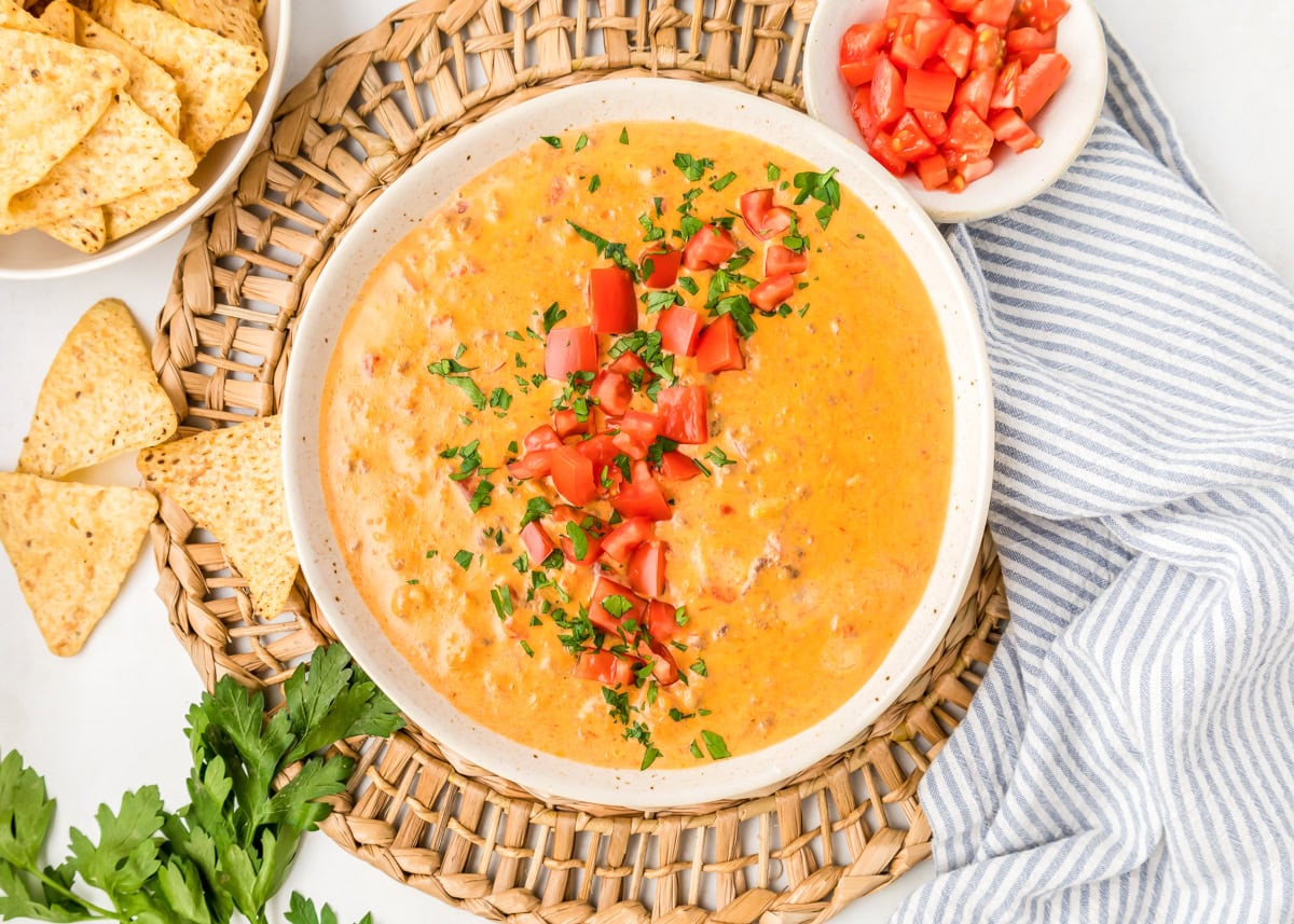 Hamburger dip recipe in white bowl with tomatoes and cilantro on top.