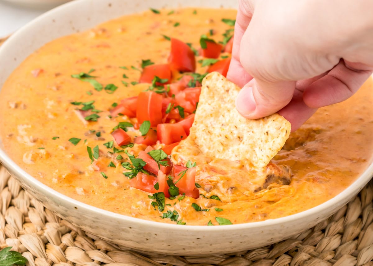 Hamburger dip served in white bowl with a tortilla chip dipped in.