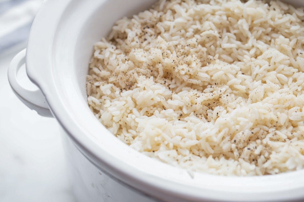 Cooked white rice in a white crockpot dish with black pepper sprinkled on top. 