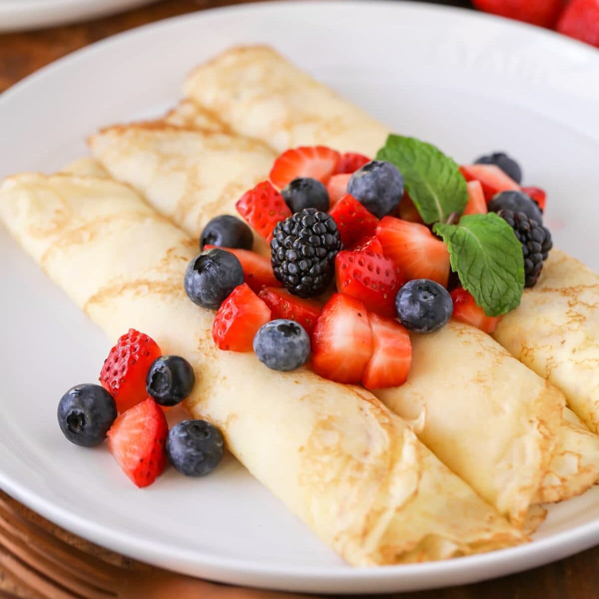 3 Rolled Swedish Pancakes with berries on top on white plate.