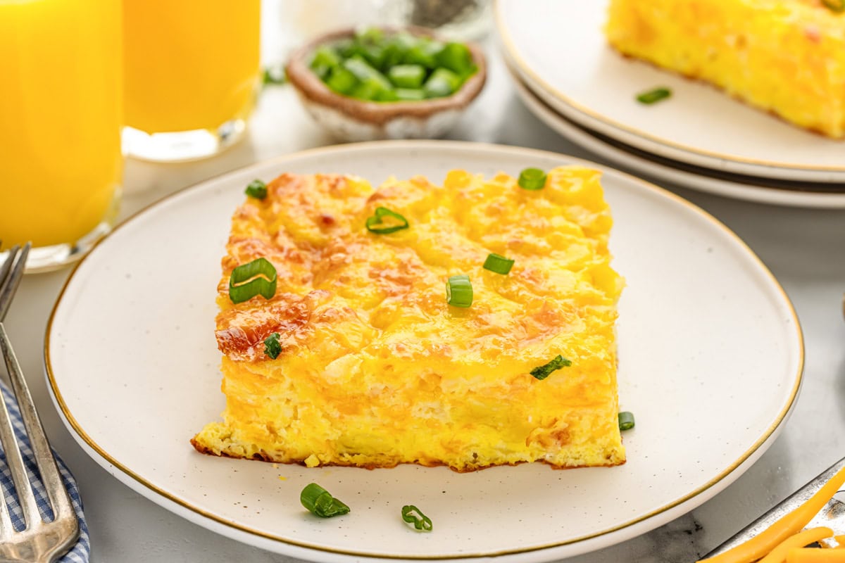 A slice of baked eggs casserole on a white plate topped with green onions.