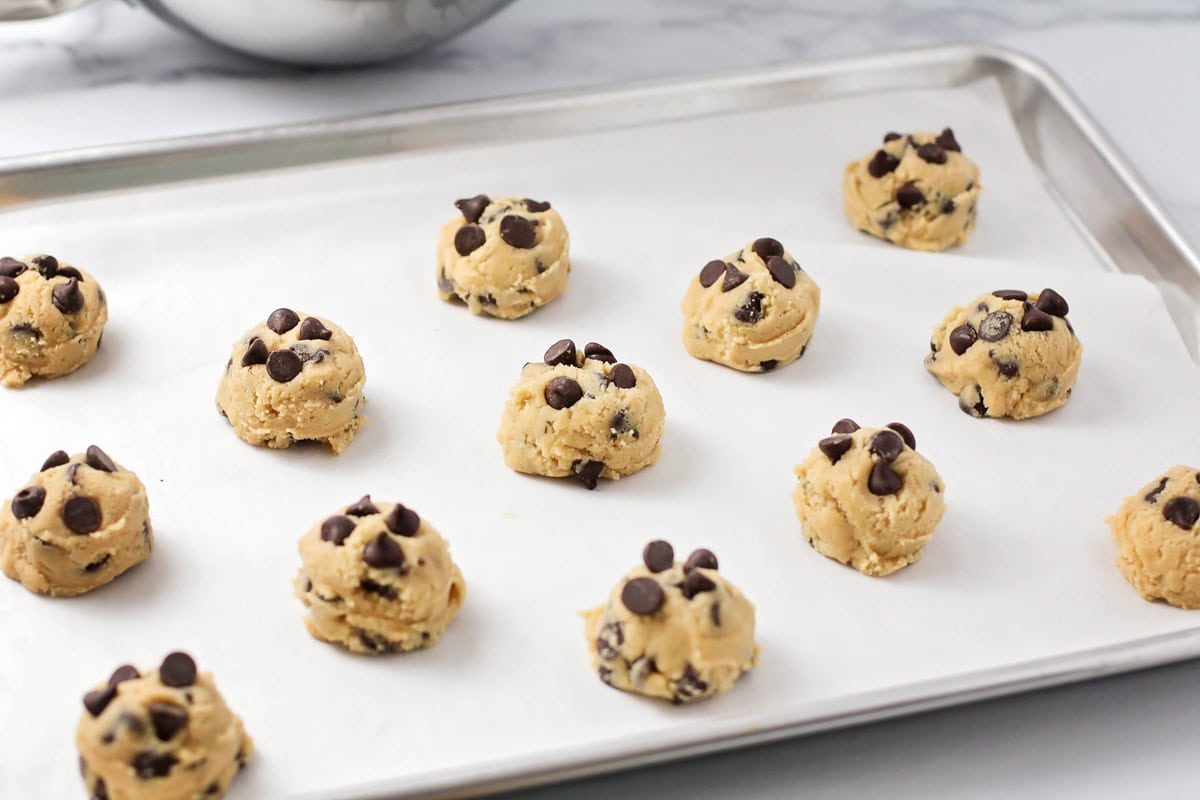 Chocolate chip cookie dough balls on a lined baking sheet ready to be baked.