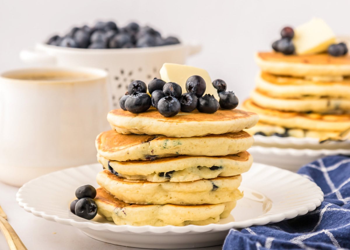 A stack of blueberry pancakes on a white plate topped with fresh blueberries.