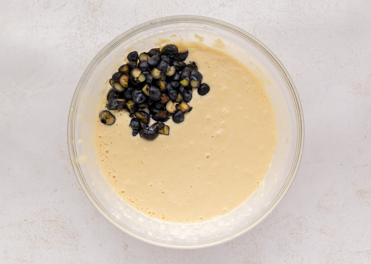 Adding blueberries to pancake batter in a glass bowl.