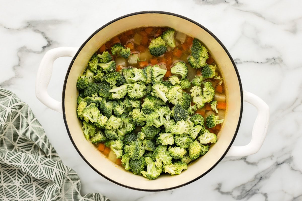 Broccoli poured into pot with other ingredients for soup.