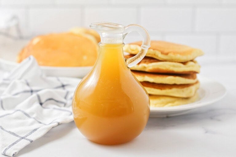 Buttermilk syrup recipe in pitcher near pancakes on plate.