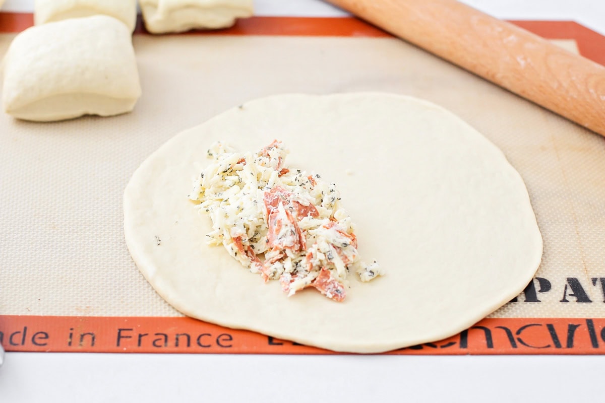 Adding cheese and pepperoni to the center of a dough circle.