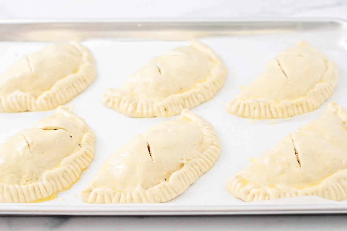 Six calzones on a lined baking sheet.