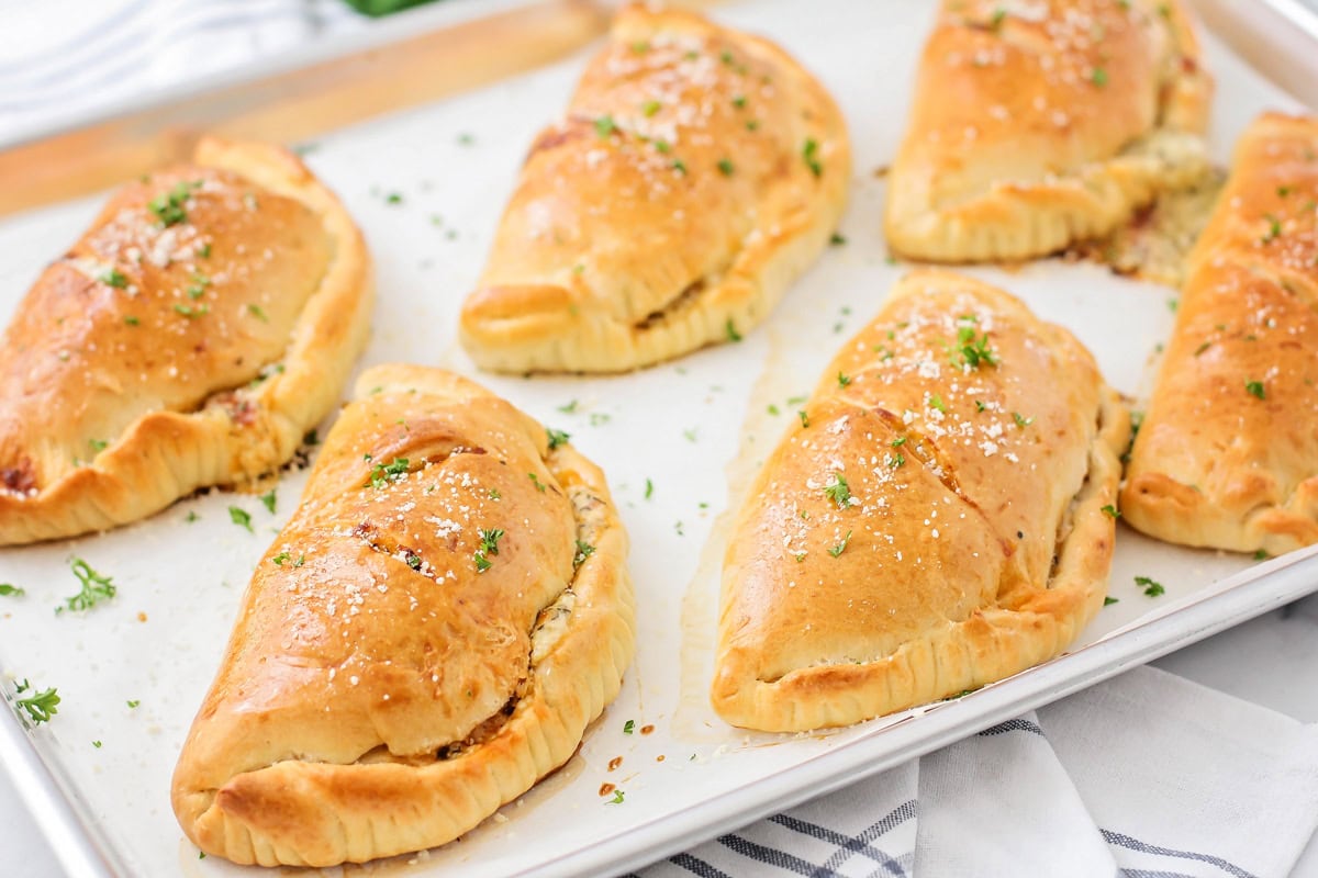 Calzone recipe - six baked on a lined sheet pan and topped with fresh herbs.