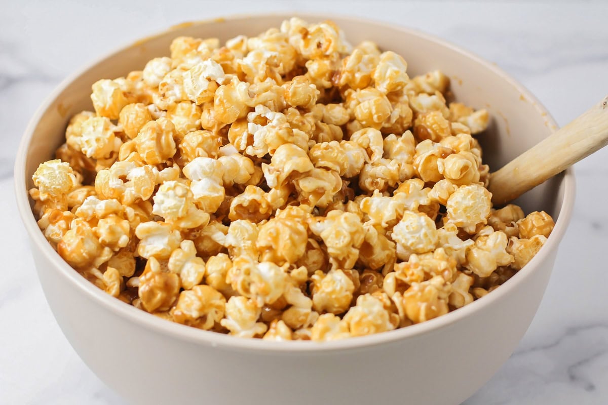 Adding popcorn to caramel mixture in a mixing bowl.