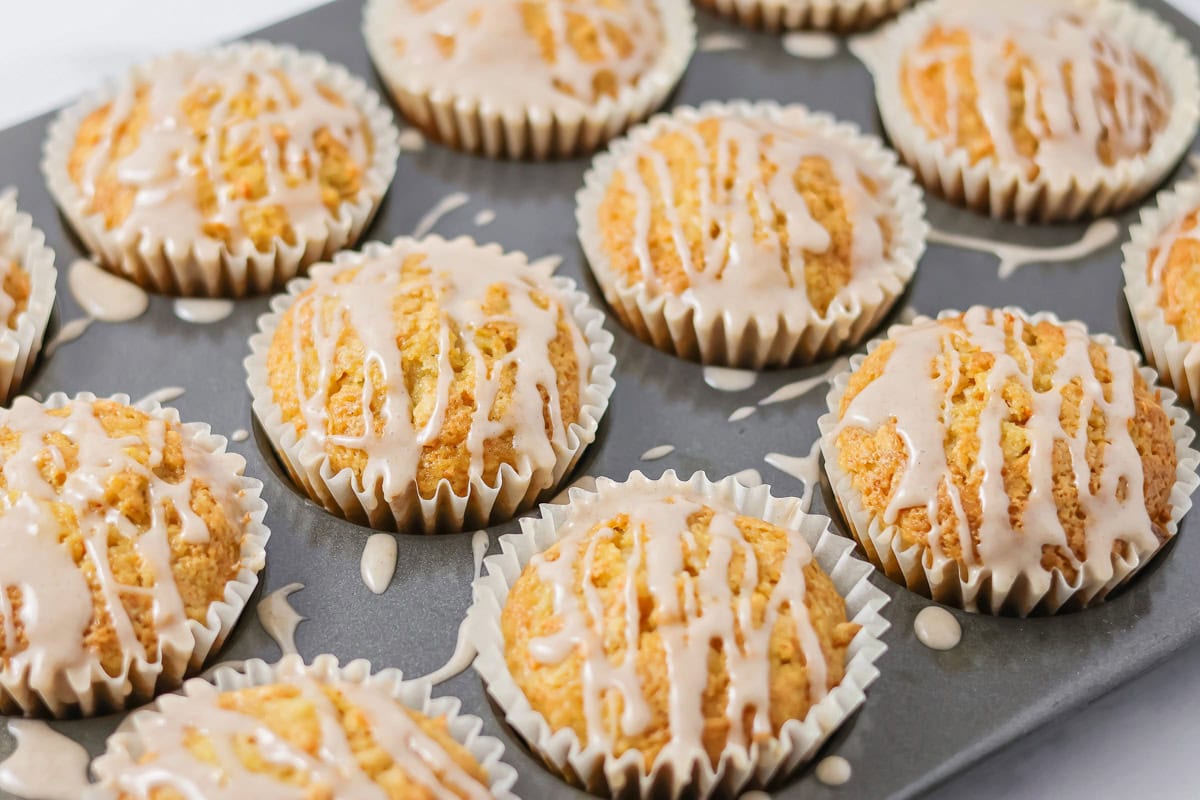 Carrot cake muffins in a tin topped with cinnamon glaze.