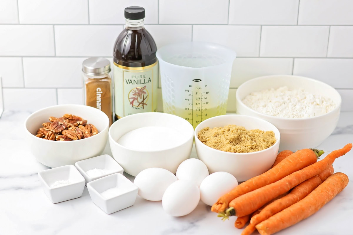 Flour, sugar, carrots, eggs, pecans, and other ingredients on a kitchen counter.