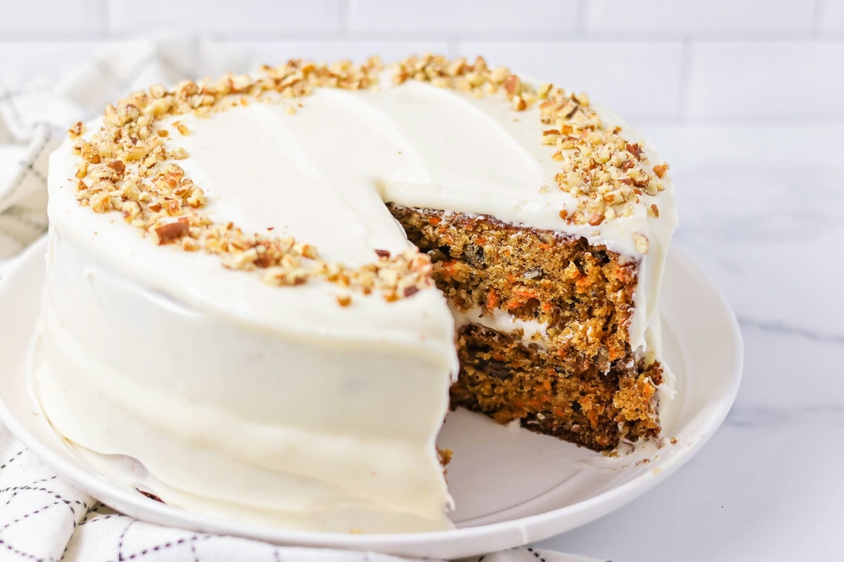 A frosted homemade carrot cake with a slice missing.