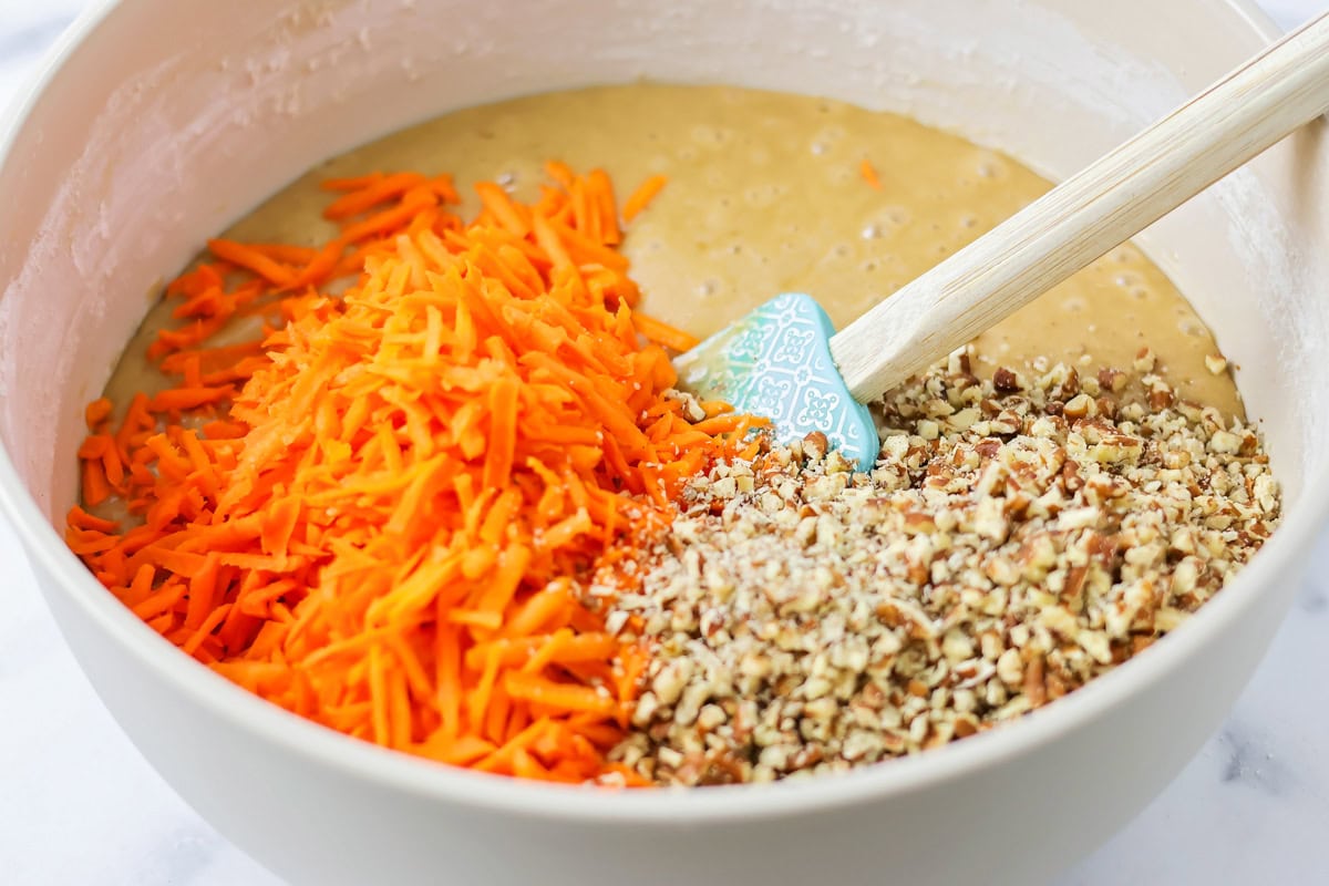 Adding carrots and chopped nuts to cake batter in a bowl.