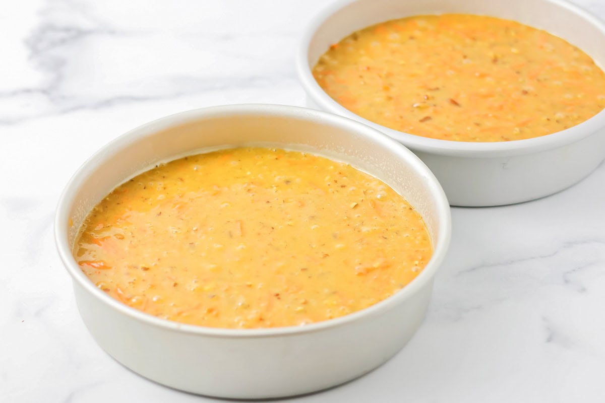 Two cake pans filled with batter on a kitchen counter.