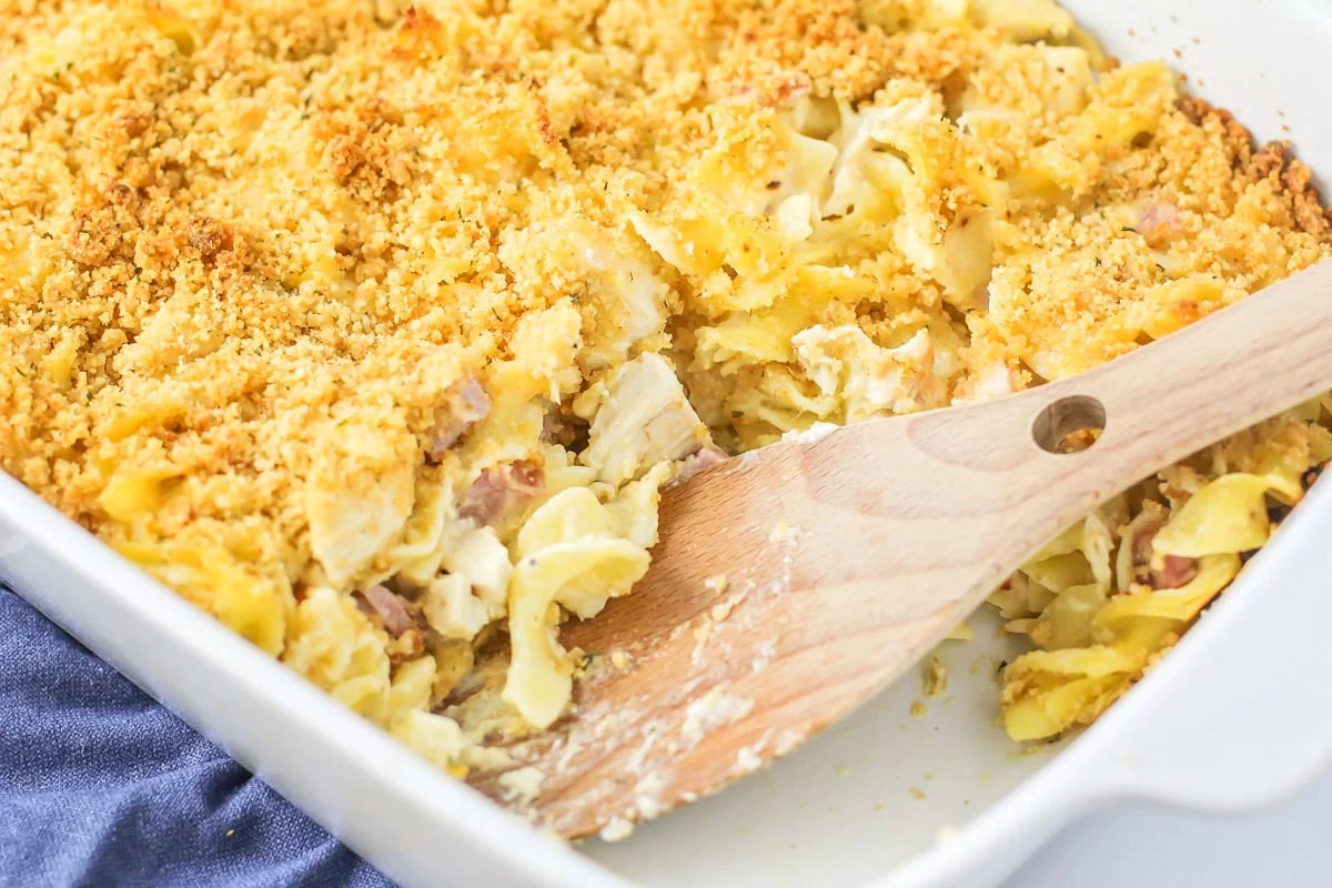 Scooping chicken cordon bleu casserole from a baking dish.