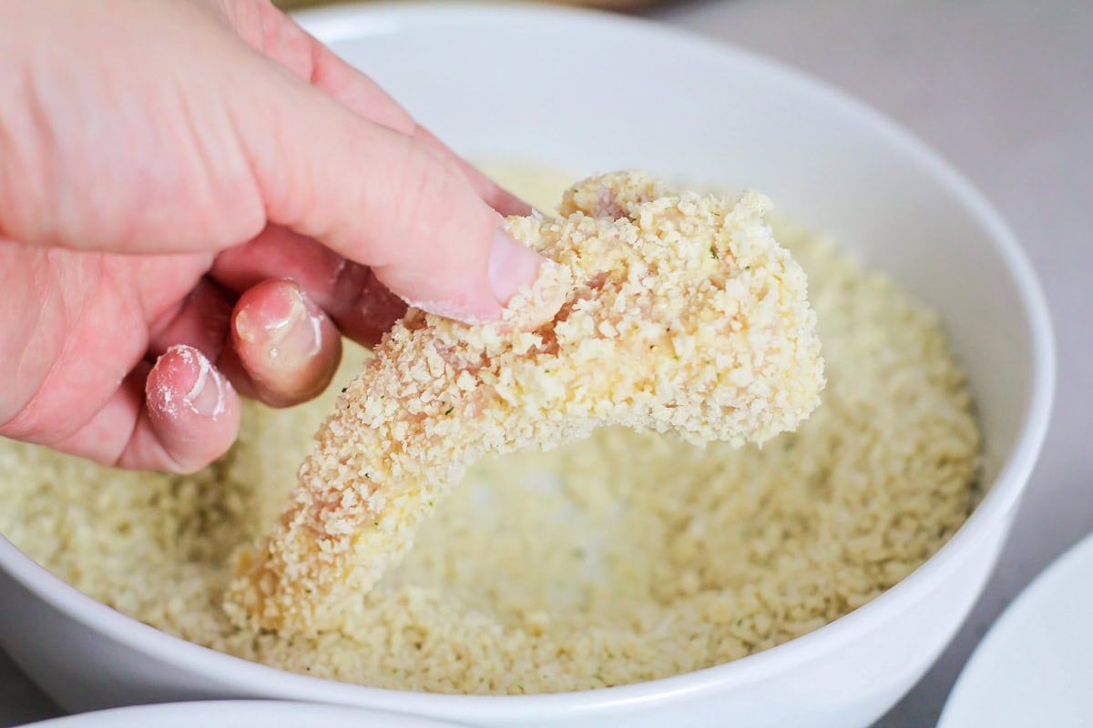 Chicken breast being dipped into Panko.