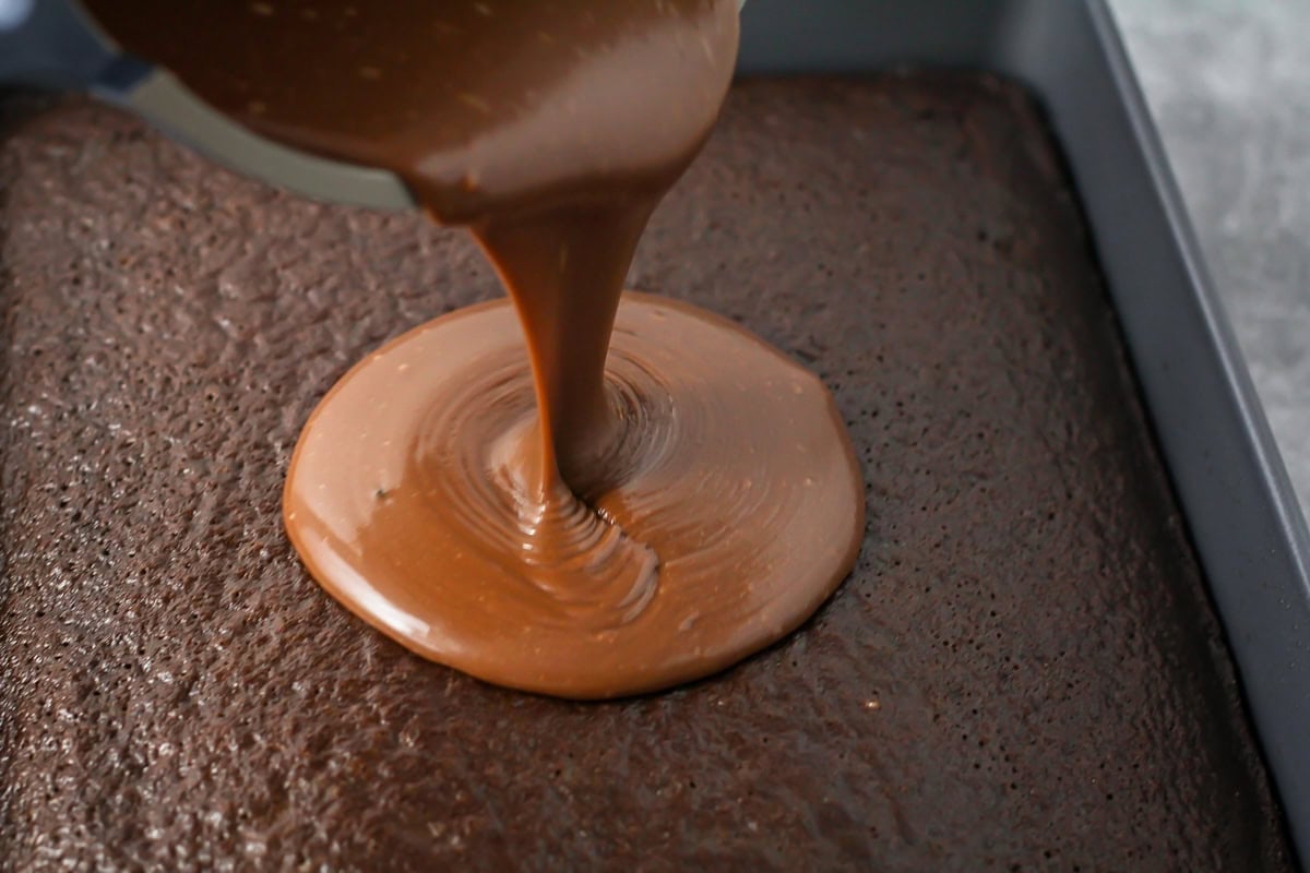 Pouring frosting on a baked sheet cake.