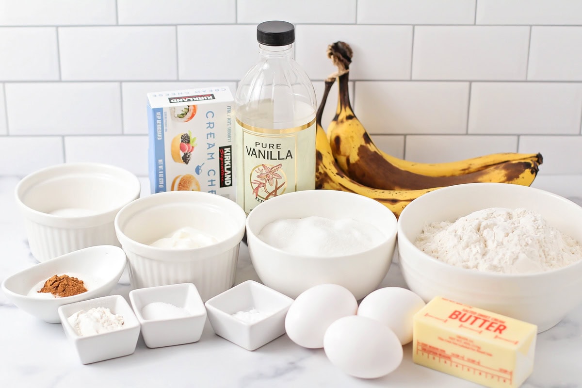 Our no-yeast cream cheese banana bread is a delicious twist on a classic with a sweet and tangy center and cinnamon sugar crust. Eggs, bananas, sugar, flour, and other ingredients on a kitchen counter.