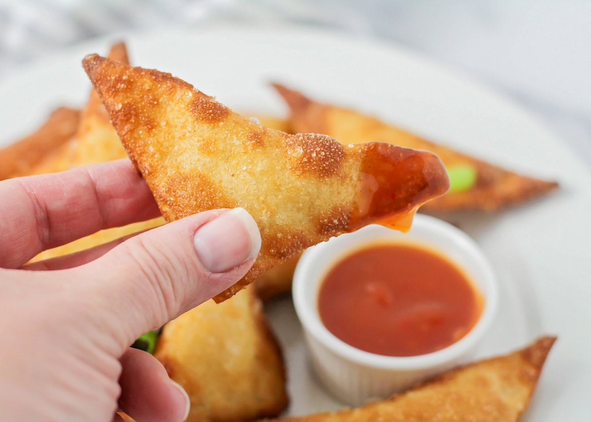 Close up of dipped cream cheese wontons served with sauce.