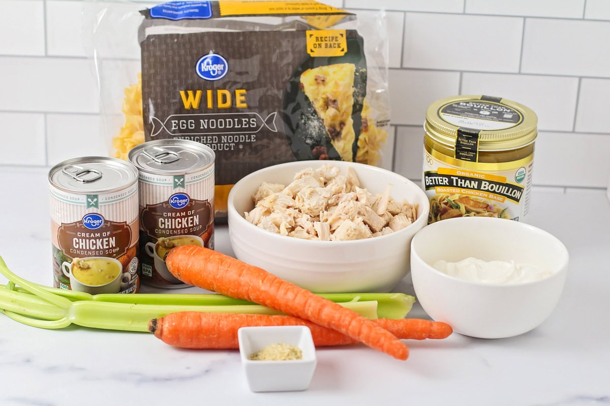 Egg noodles, diced chicken, veggies, and soup cans on a kitchen counter.