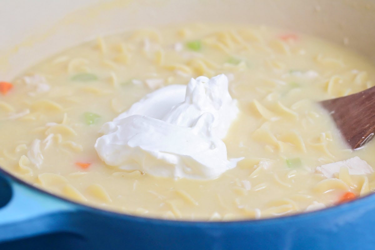 Adding sour cream to chicken soup in a dutch oven.