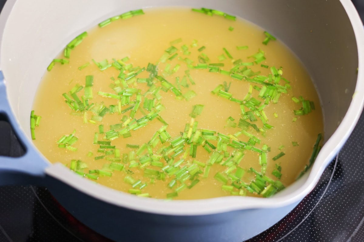 Chicken broth and green onions simmering in a large pot.