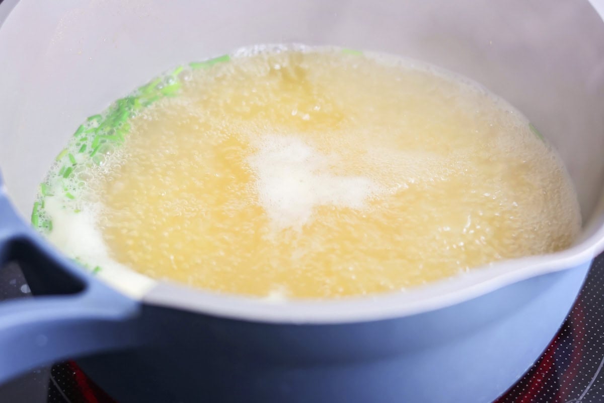 Chicken broth and green onions simmering in a large pot.