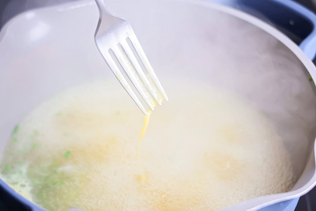 Drizzling egg mixture into boiling broth for egg drop soup.