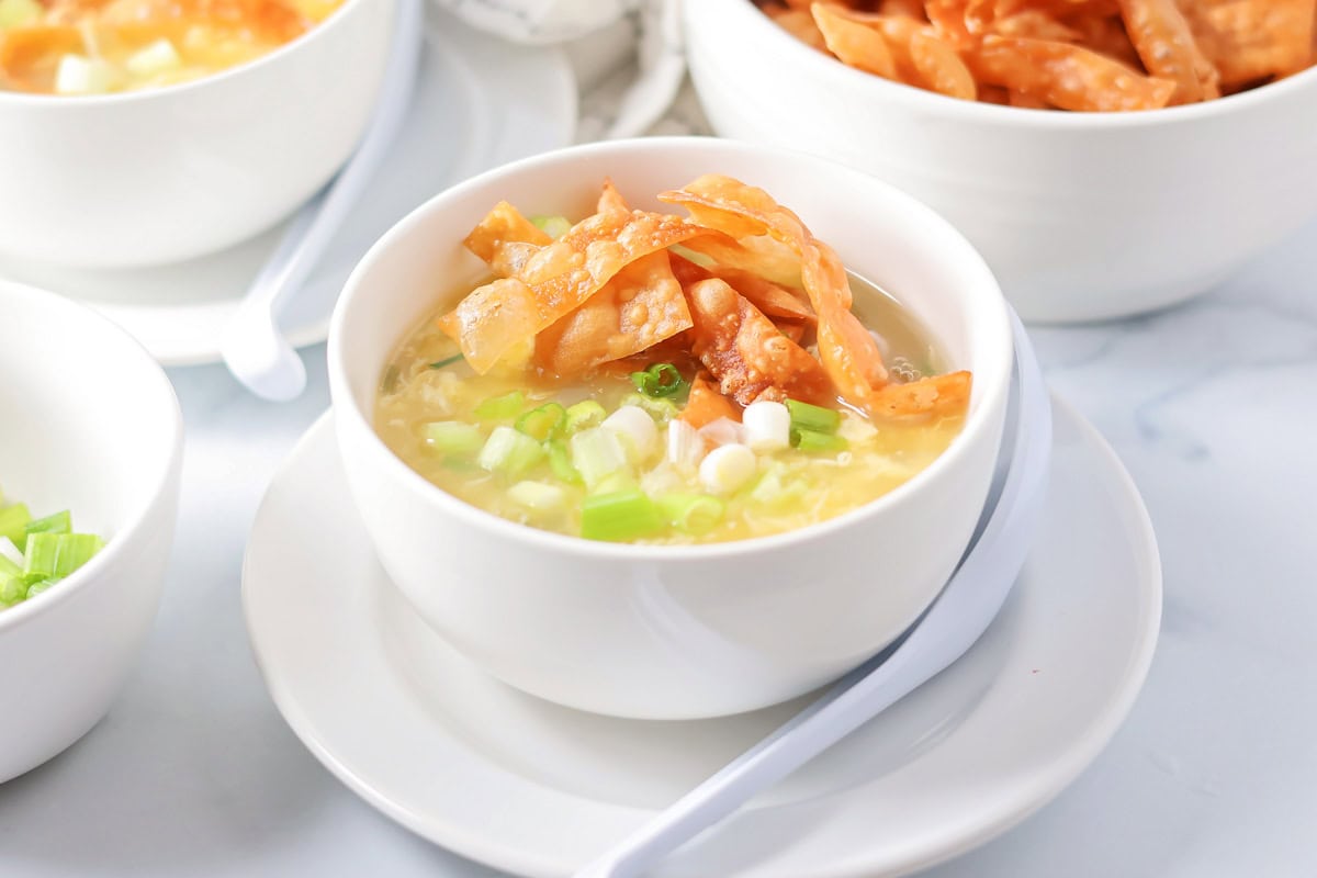 Homemade egg drop soup in a small soup bowl topped with crispy wonton strips.