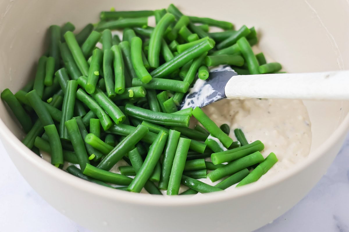 Adding green beans to cream of mushroom soup in a mixing bowl.