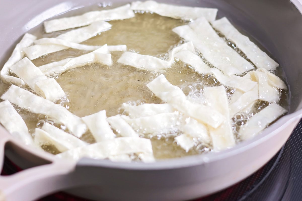 Wonton strips frying in a pot of oil.