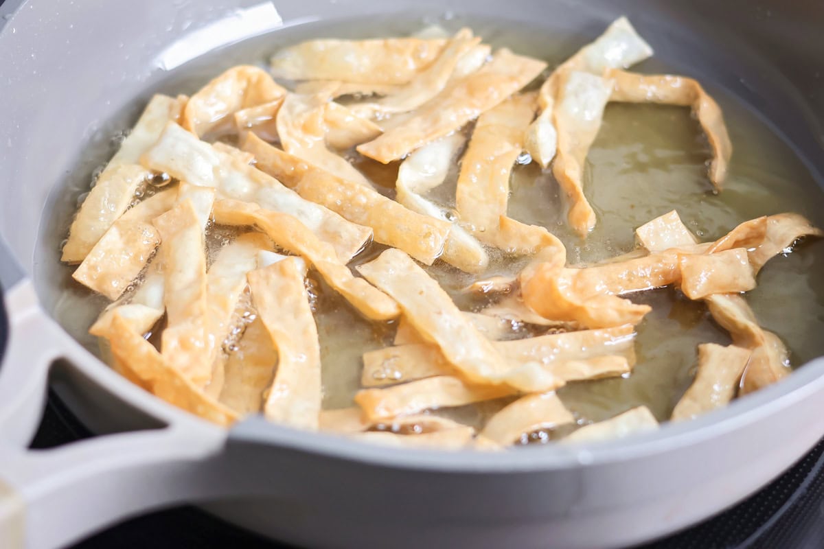 Wonton strips frying in a pan of oil.