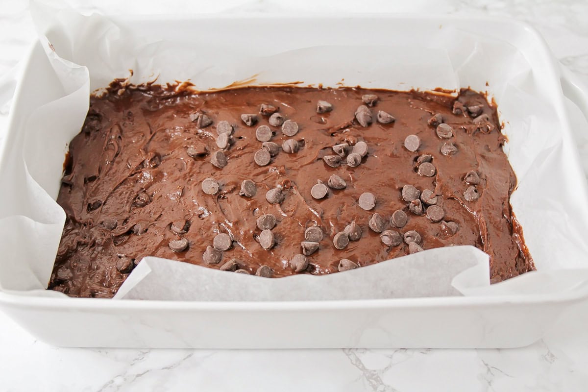 Brownie batter and chocolate chips spread into baking dish.