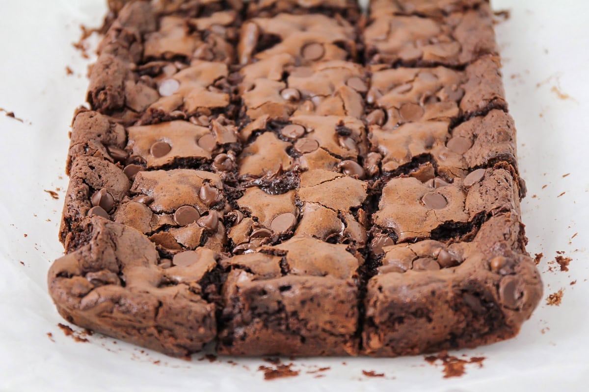 Homemade brownies cut up into squares on parchment paper.