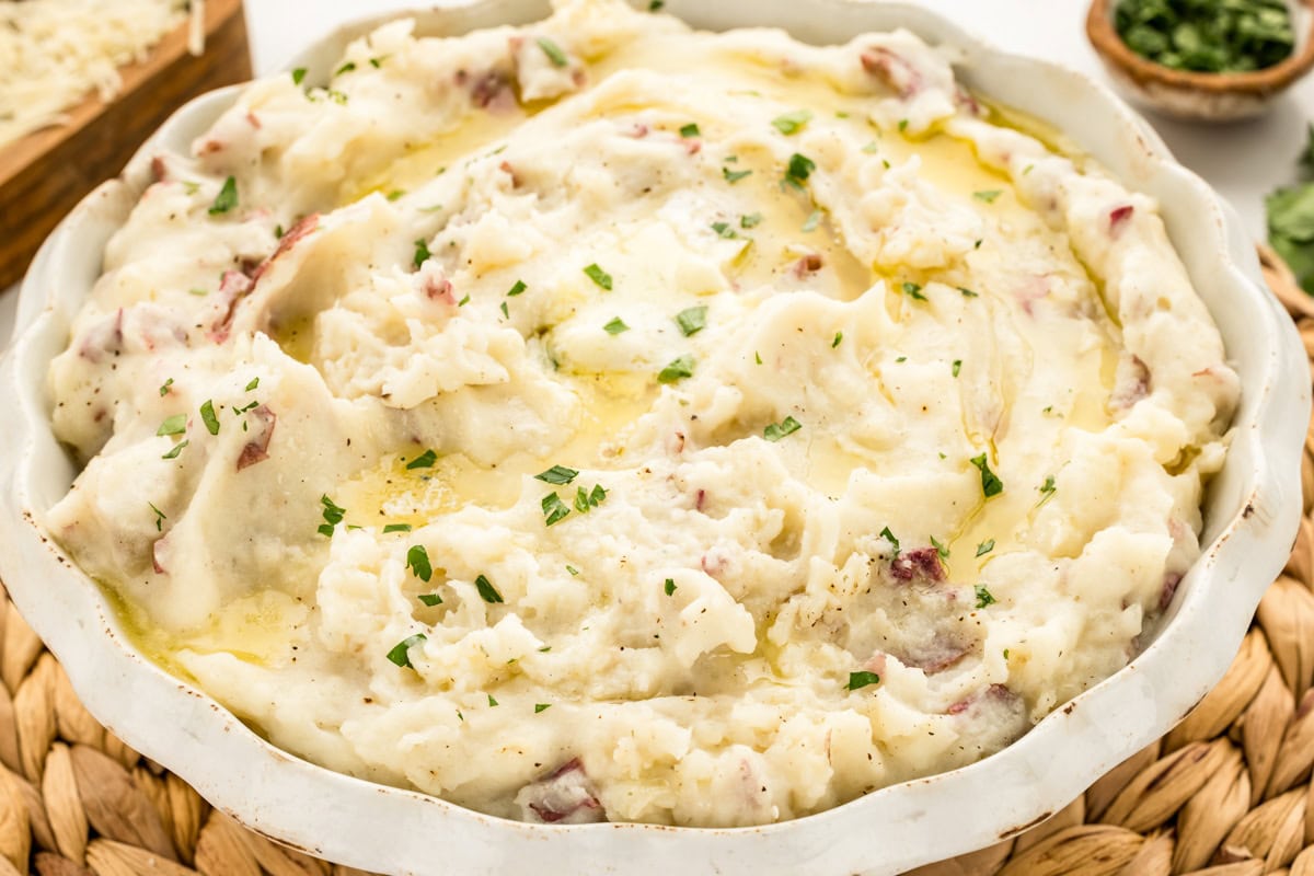 Red mashed potatoes served in a white bowl topped with a pat of butter.