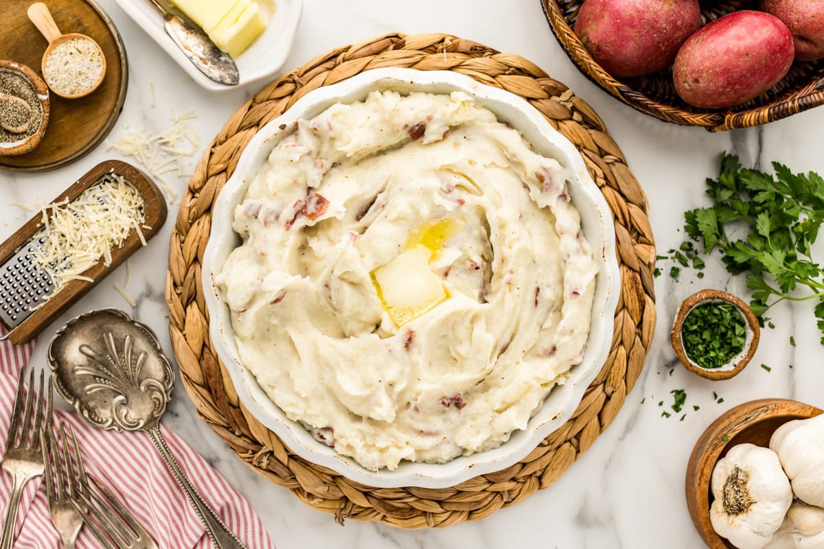 Red mashed potatoes served in a white bowl topped with a pat of butter.