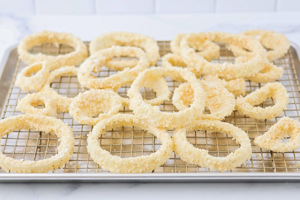 Coated onion rings on a wire rack on a sheet pan.