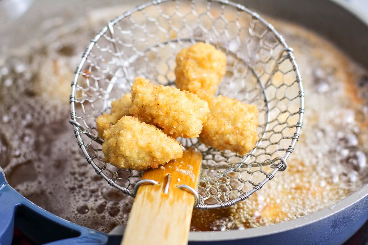 Spooning fried chicken pieces from the oil.