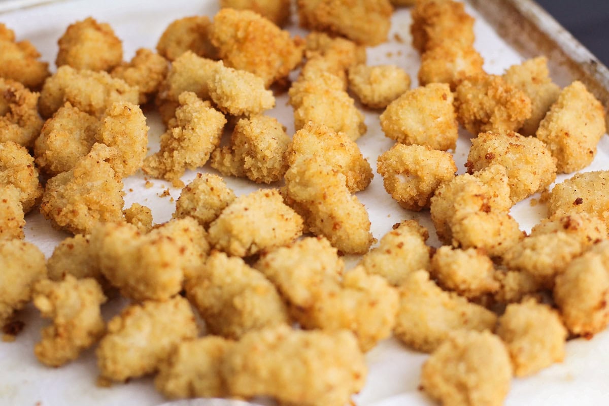 Fried popcorn chicken on a paper towel lined baking sheet.